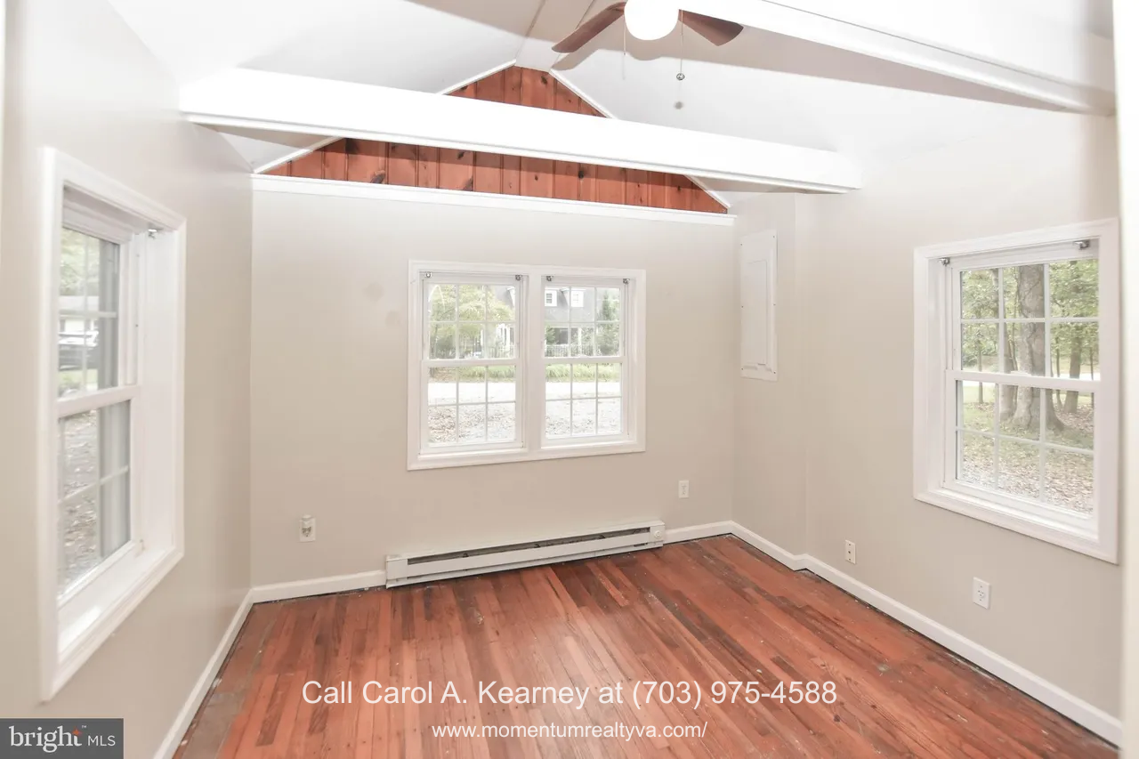 420 White Oak Ln 6 Bedroom inside the 420 White Oak Ln, Bluemont, VA home for sale, featuring original hardwood floors, neutral-colored walls, multiple large windows with wooded views, and exposed white ceiling beams with a ceiling fan.