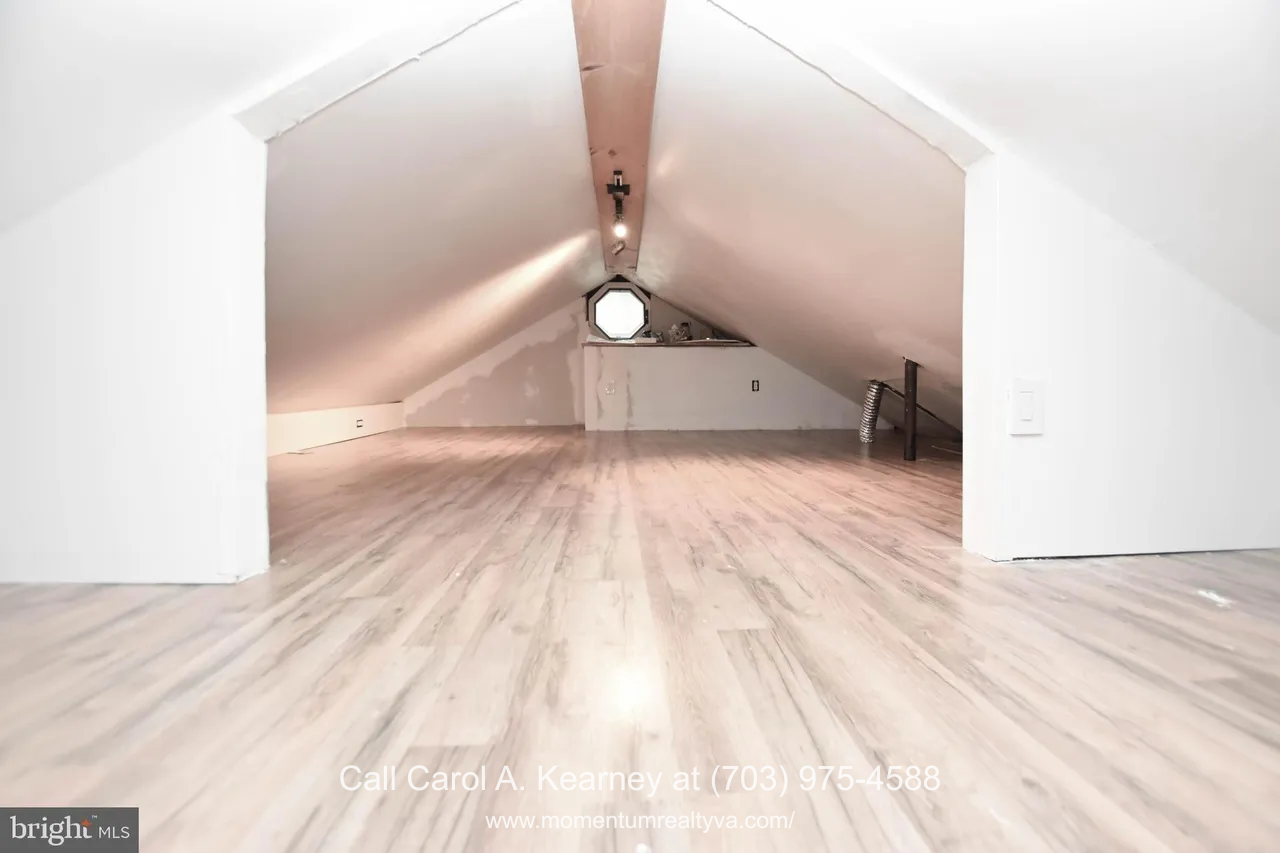 420 White Oak Ln 9 Finished loft storage area inside the 420 White Oak Ln, Bluemont, VA home for sale, showing a long, low-ceilinged space with light wood flooring, white walls, and a small octagon window at the far end.