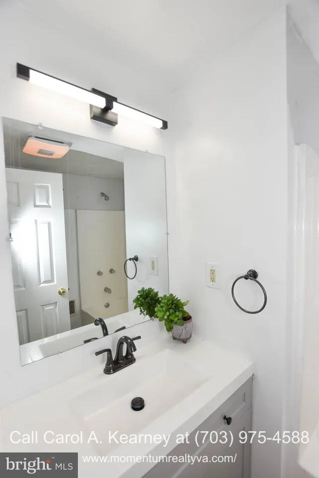 420 White Oak Ln 1 Bathroom inside the 420 White Oak Ln, Bluemont, VA home for sale, featuring a modern white vanity with black hardware, a large mirror with contemporary lighting, white walls, and a glimpse of the shower and door in the reflection.
