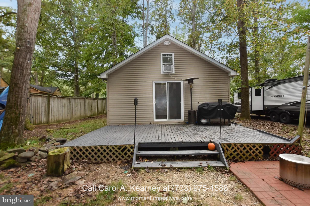 420 White Oak Ln 4 Rear exterior of the 420 White Oak Ln, Bluemont, VA home for sale, featuring a spacious wooden deck with steps, sliding glass doors, outdoor grill setup, and a wooded backyard surrounded by tall trees.