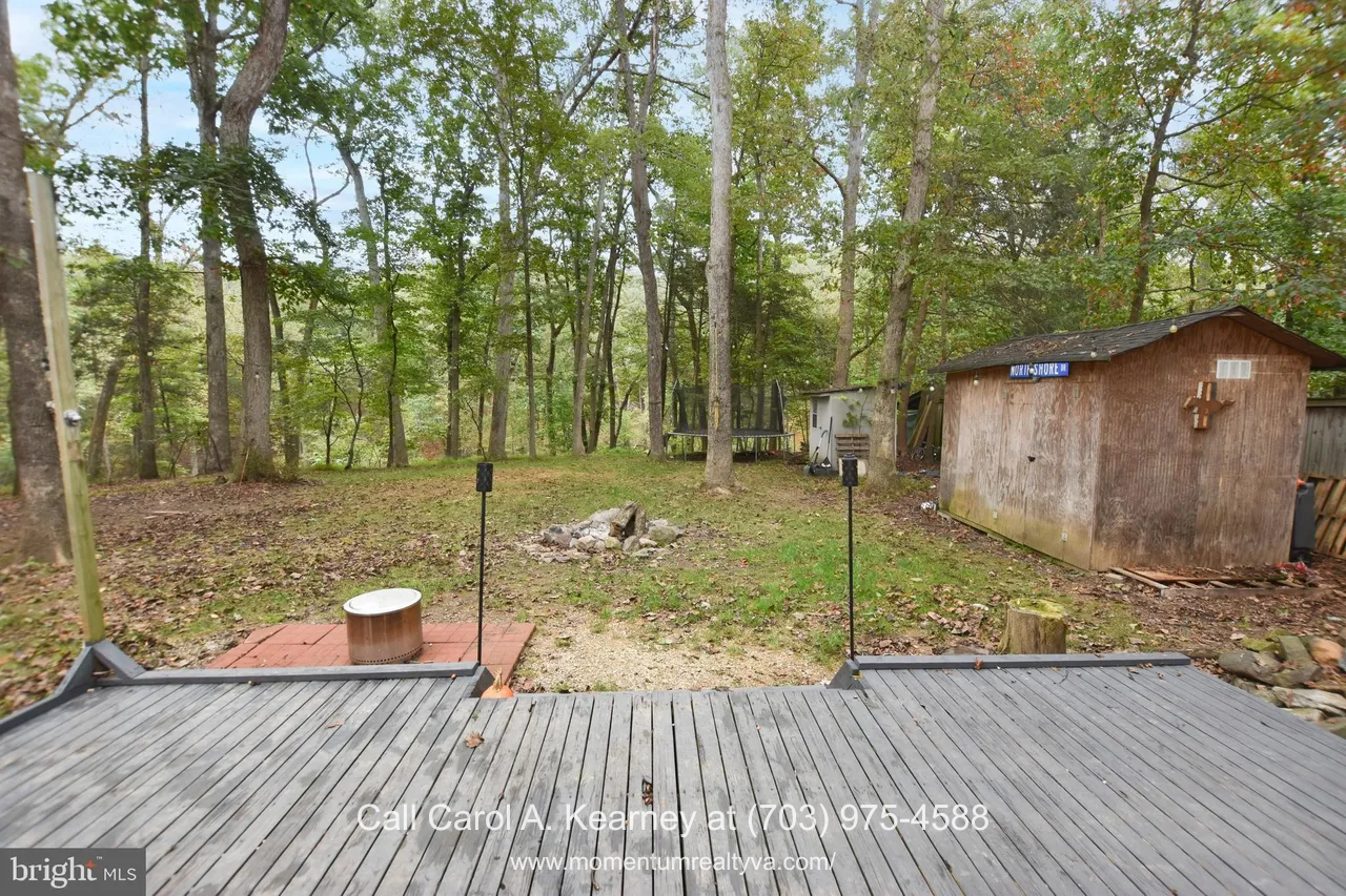 420 White Oak Ln 23 Backyard view of the 420 White Oak Ln, Bluemont, VA home for sale, showing a spacious wooded lot with a firepit area, large storage shed, open grassy space, and a deck overlooking the trees.