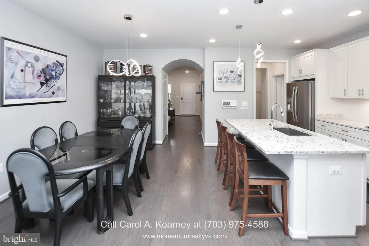 Open dining and kitchen area at 19873 Silvery Blue Ter in Ashburn, VA, featuring a quartz island with seating, pendant lighting, stainless steel appliances, hardwood floors, and an open layout ideal for everyday living in the Lexington 7 55+ community.