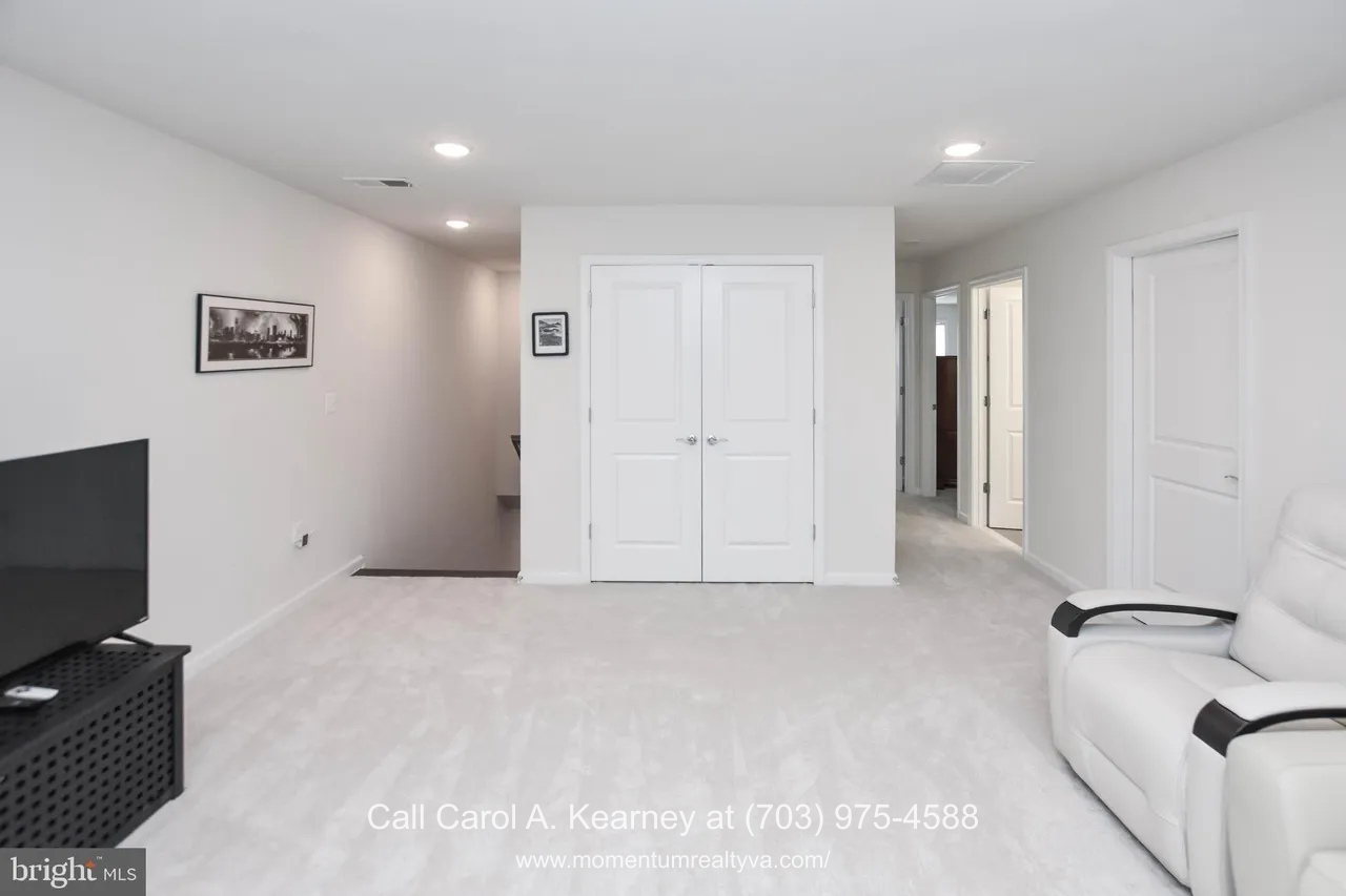 Finished lower-level family room at 19873 Silvery Blue Ter in Ashburn, VA, featuring plush carpeting, recessed lighting, neutral walls, and a spacious open layout ideal for flexible living in the Lexington 7 55+ community.