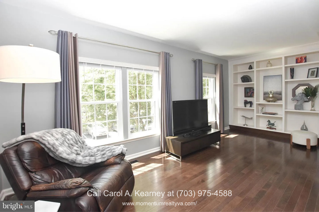 Custom Built-In Living Room – 25474 Brickell Dr Bright living room at 25474 Brickell Dr in South Riding, Chantilly, VA, featuring hardwood floors, large windows, and custom built-in bookshelves.