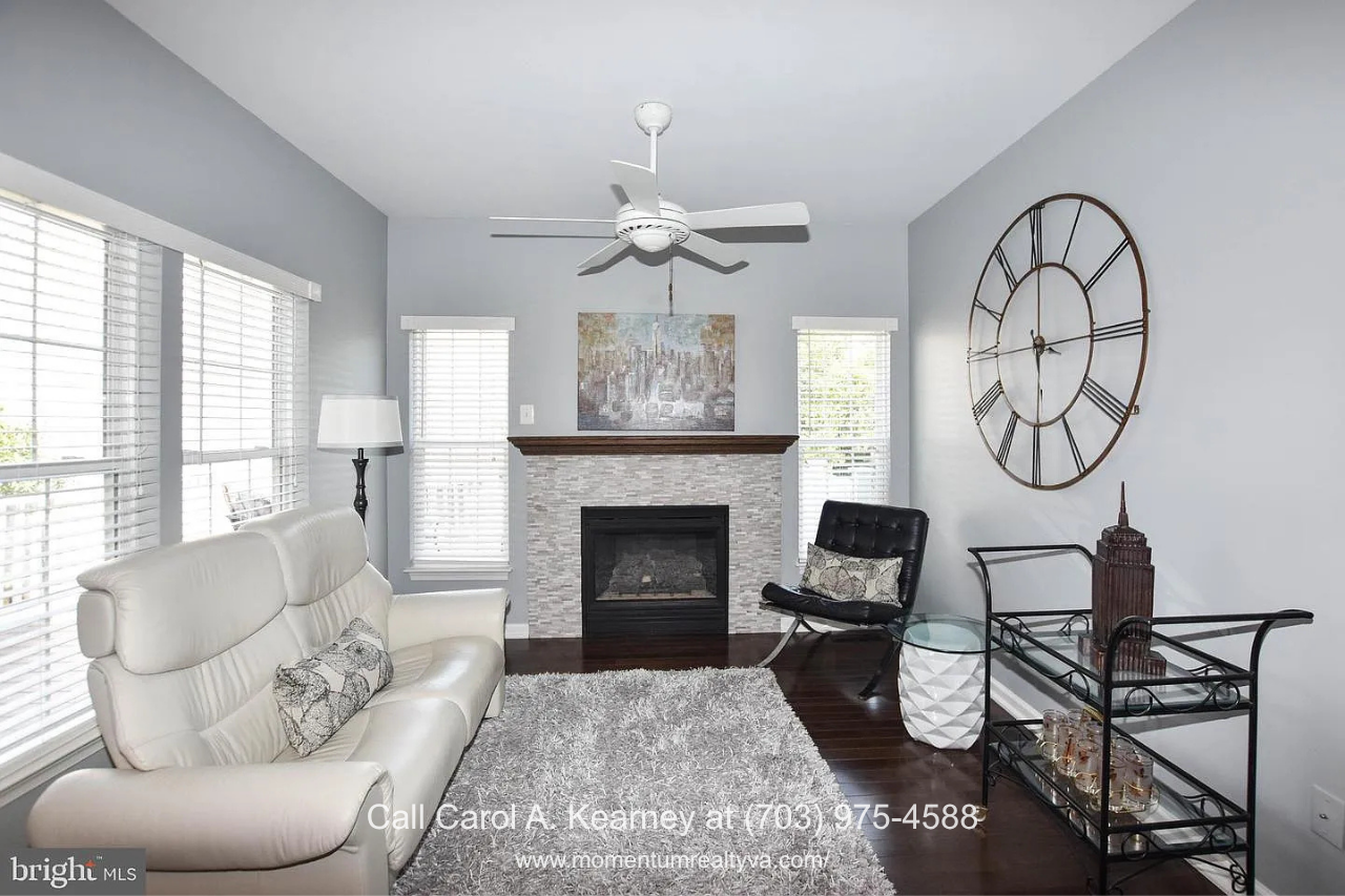 Family Room with Gas Fireplace – 25474 Brickell Dr Bright family room at 25474 Brickell Dr in South Riding, Chantilly, VA, featuring hardwood floors, a gas fireplace with custom mantel and surround, and large windows.