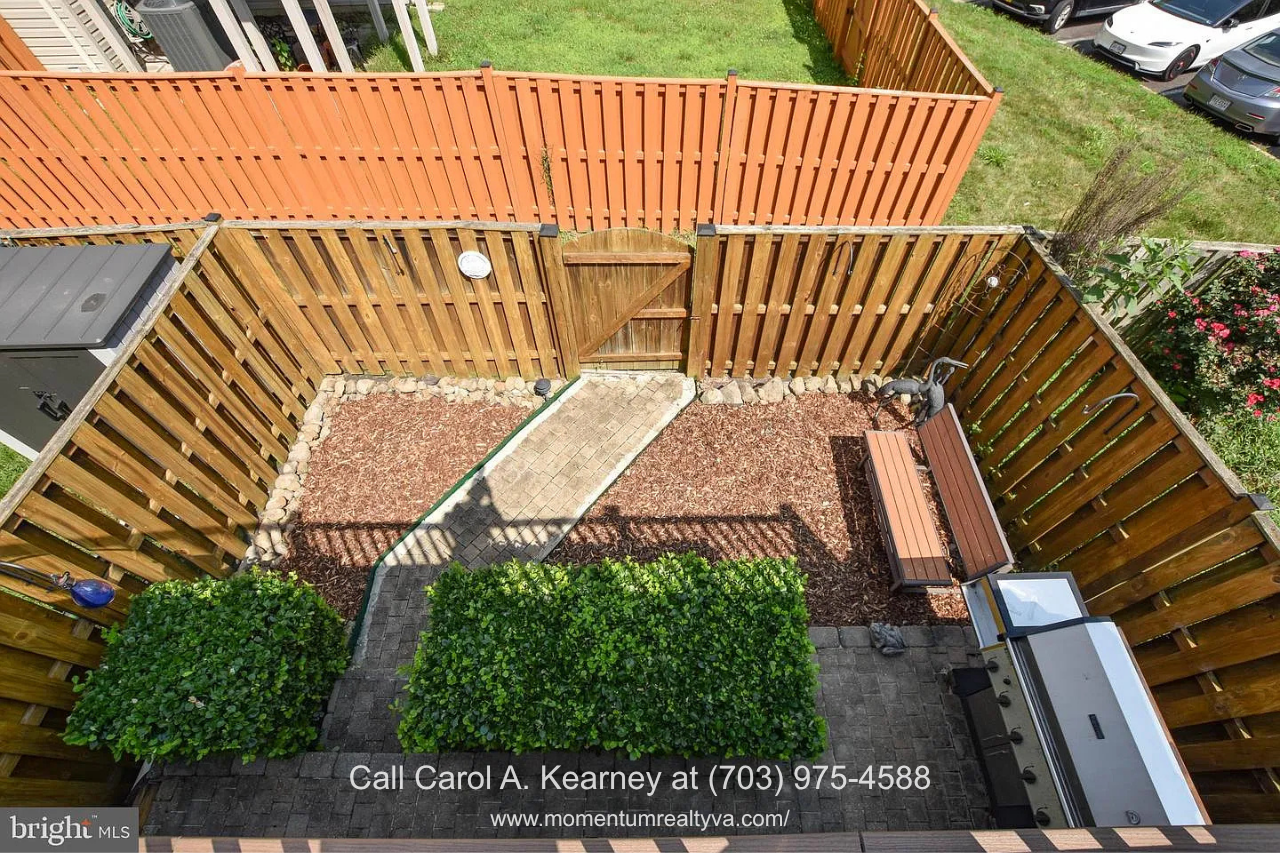 Fenced Backyard – 25474 Brickell Dr Private fenced backyard at 25474 Brickell Dr in South Riding, Chantilly, VA, featuring landscaping, a paved walkway, and outdoor living space.