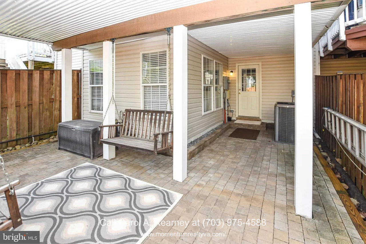 Covered Backyard Patio – 25474 Brickell Dr Covered backyard patio at 25474 Brickell Dr in South Riding, Chantilly, VA, featuring a paved outdoor living area, porch swing, and privacy fencing.
