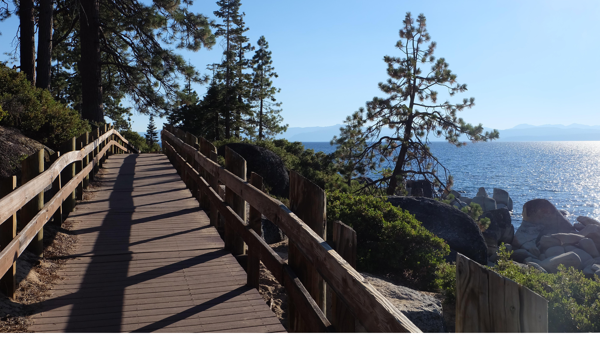 A wooden path on the East Shore Trail is framed by trees and showcases views of Lake Tahoe.