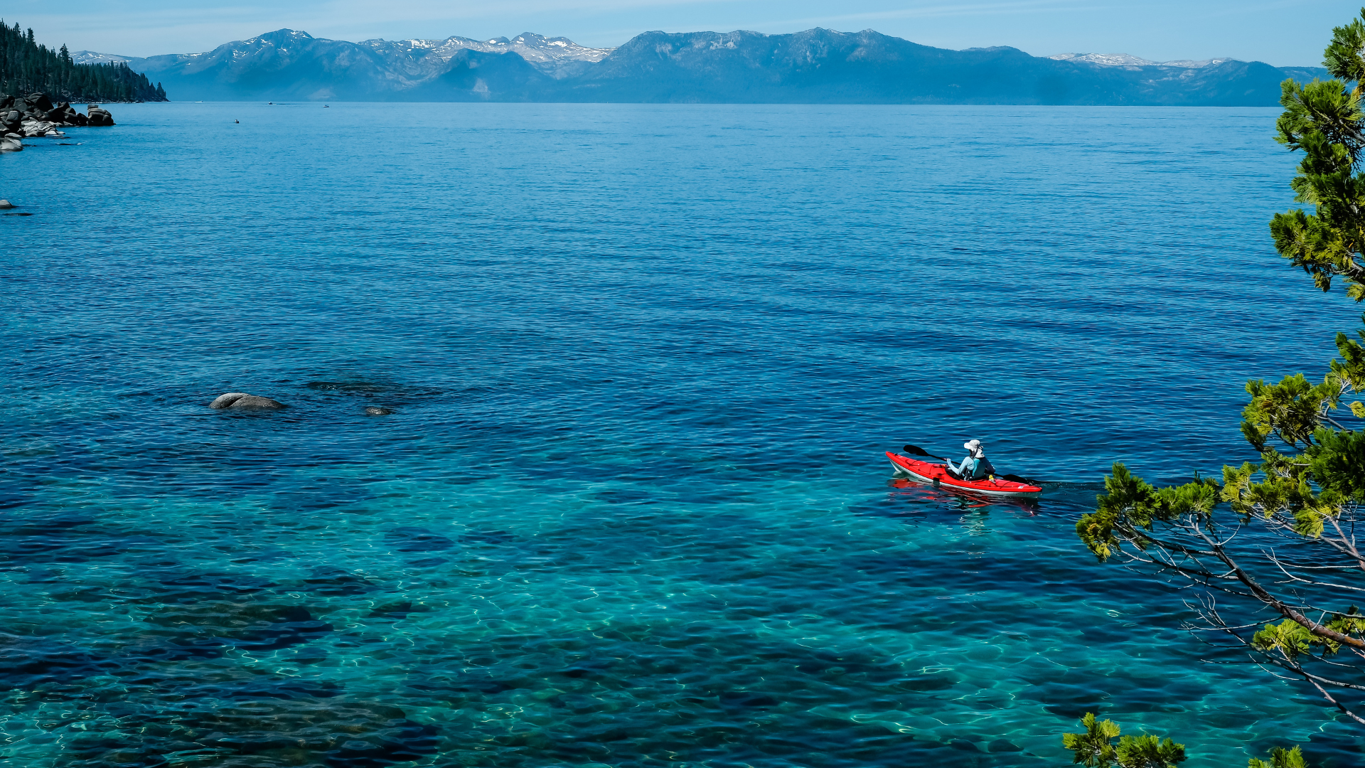 A man paddles a red canoe on surrounded by calm water and scenic views during Lake Tahoe summer vacation