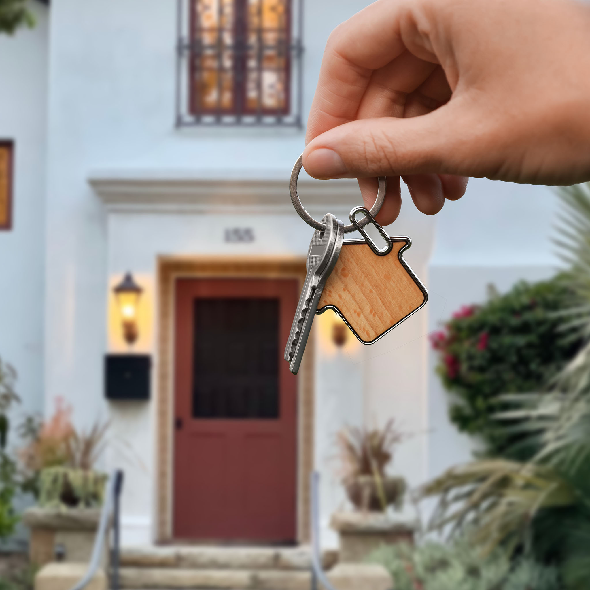 a hand holding keys in front of a santa barbara home