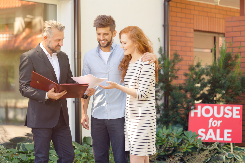 A couple with a real estate agent in front of a house