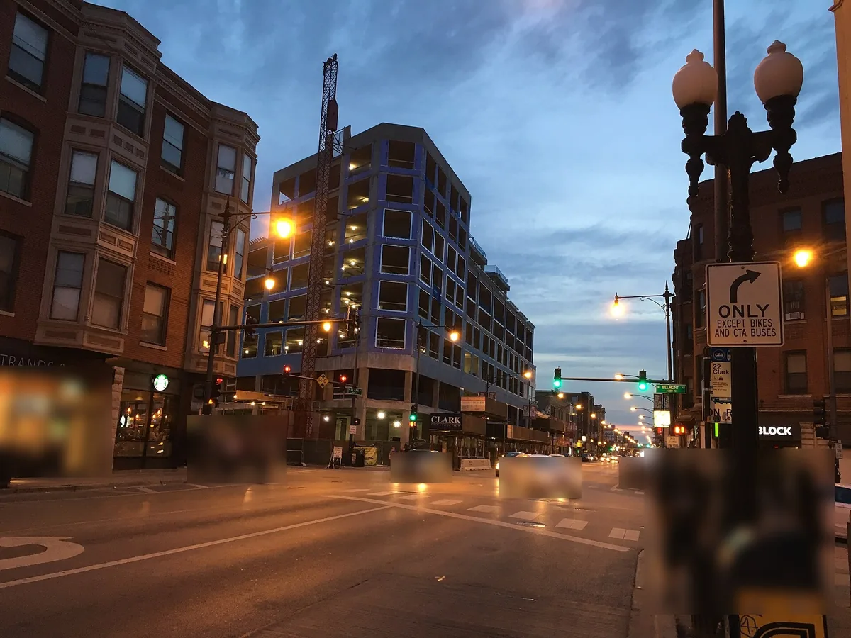 Clark Street and Belmont Avenue intersection at dusk in Lakeview East, Chicago, with street lamps and storefronts