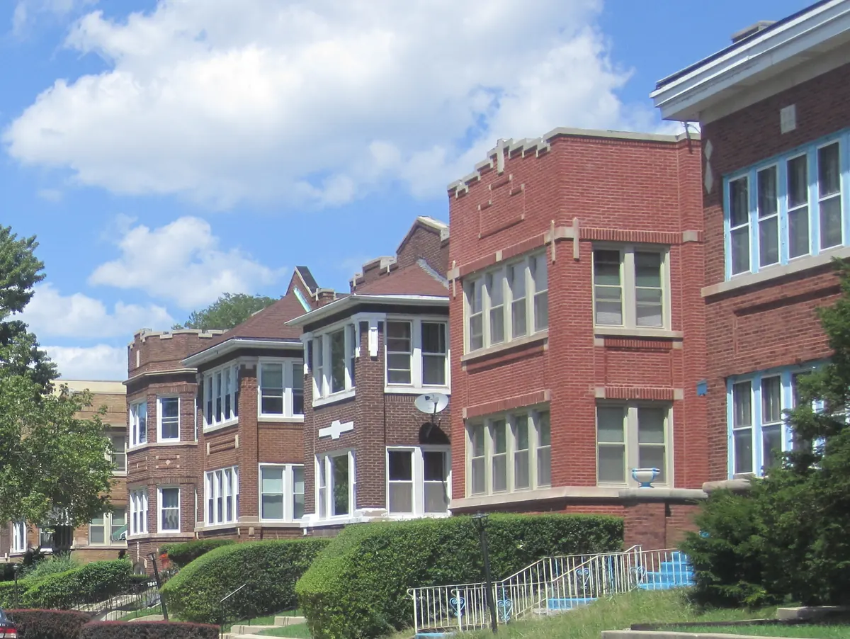 Row of red brick Chicago two-flats with bay windows, limestone trim and front lawns on a residential block in Auburn Gresham