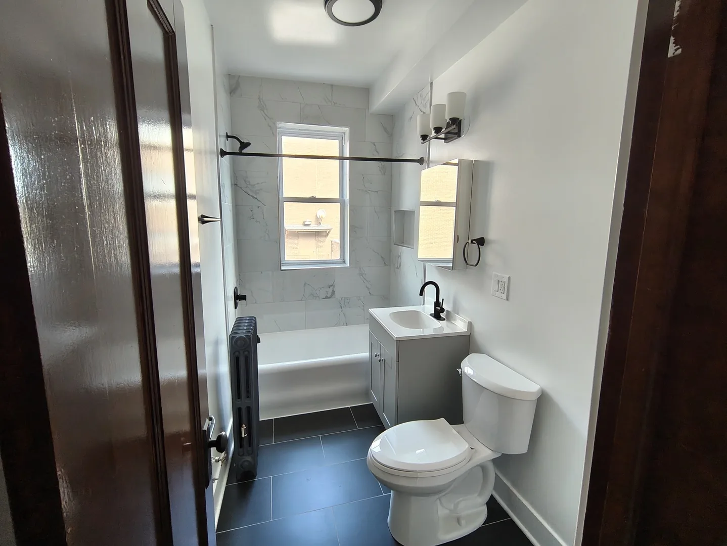 Renovated bathroom with a tub and shower, white vanity, dark tile floor and black fixtures