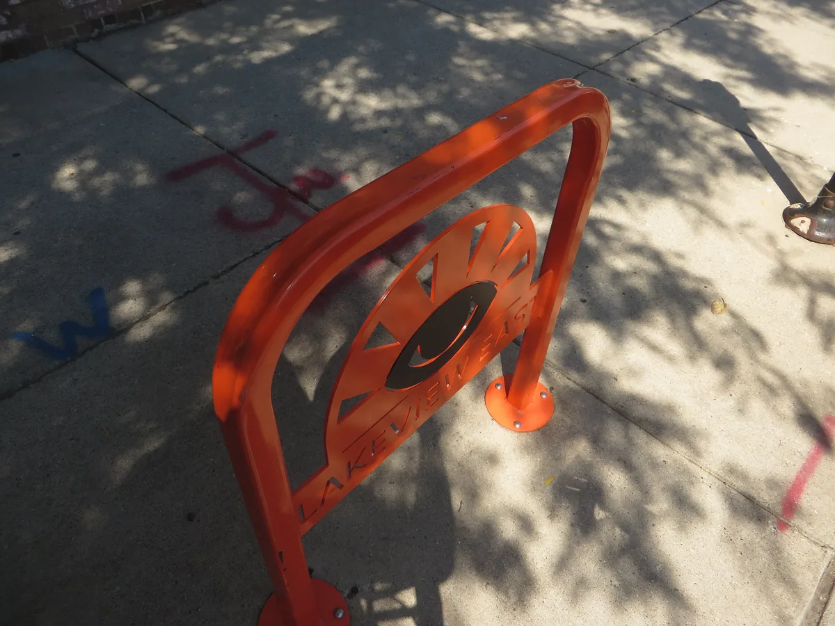 Orange sidewalk bike rack with a cut-out Lakeview East emblem in Chicago