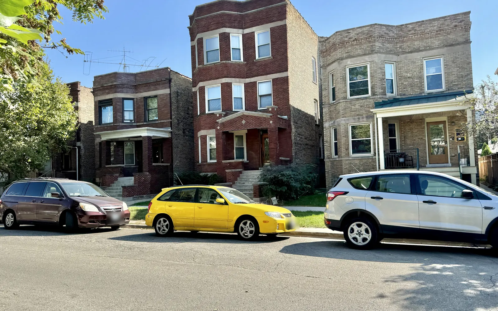 Early 20th century brick two-flats and a three-flat on Eastwood Avenue in Lincoln Square, Chicago, with cars parked at the curb