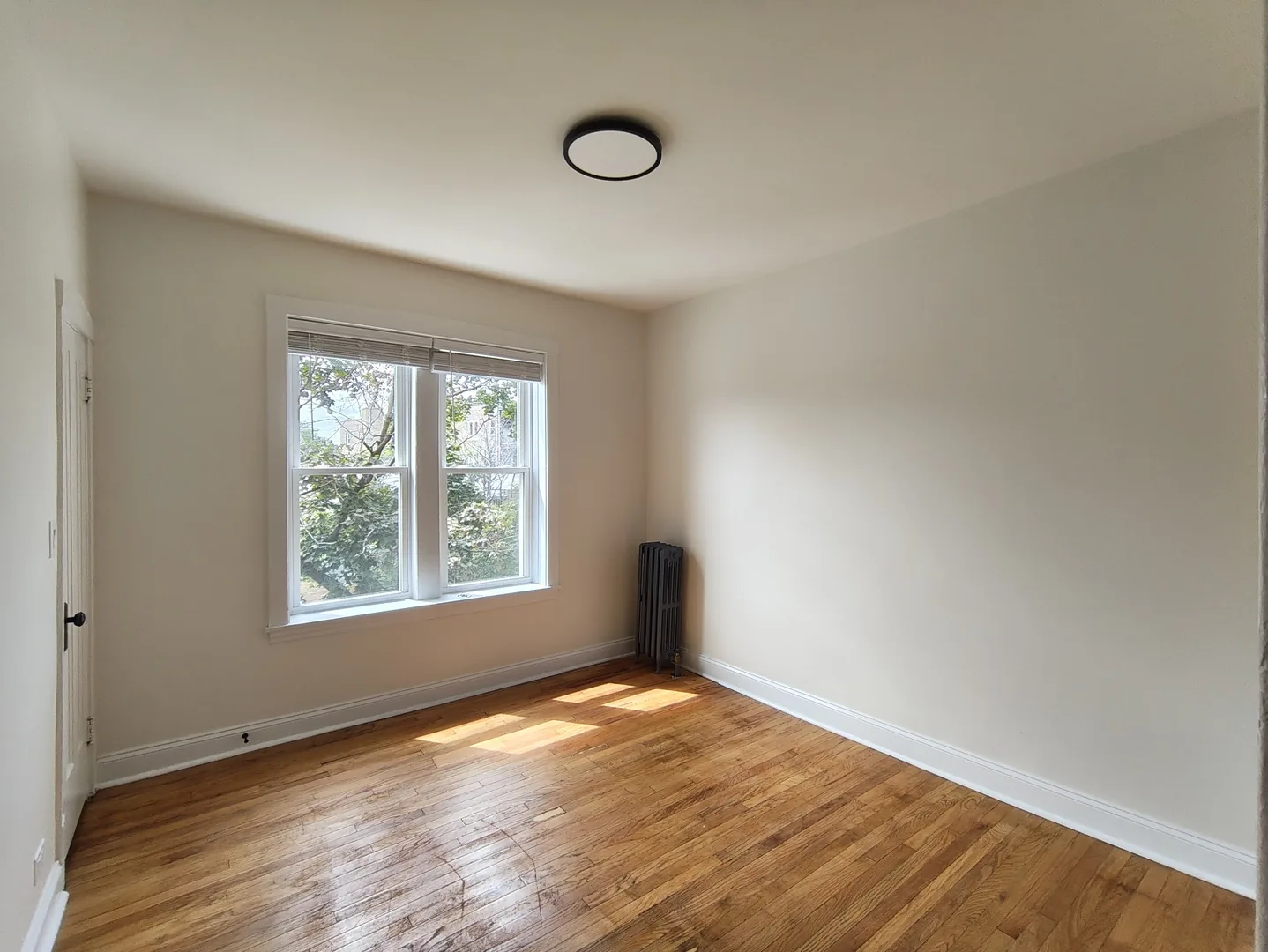 Empty bedroom with hardwood floors, a double window and a radiator in a renovated W Albion Ave apartment