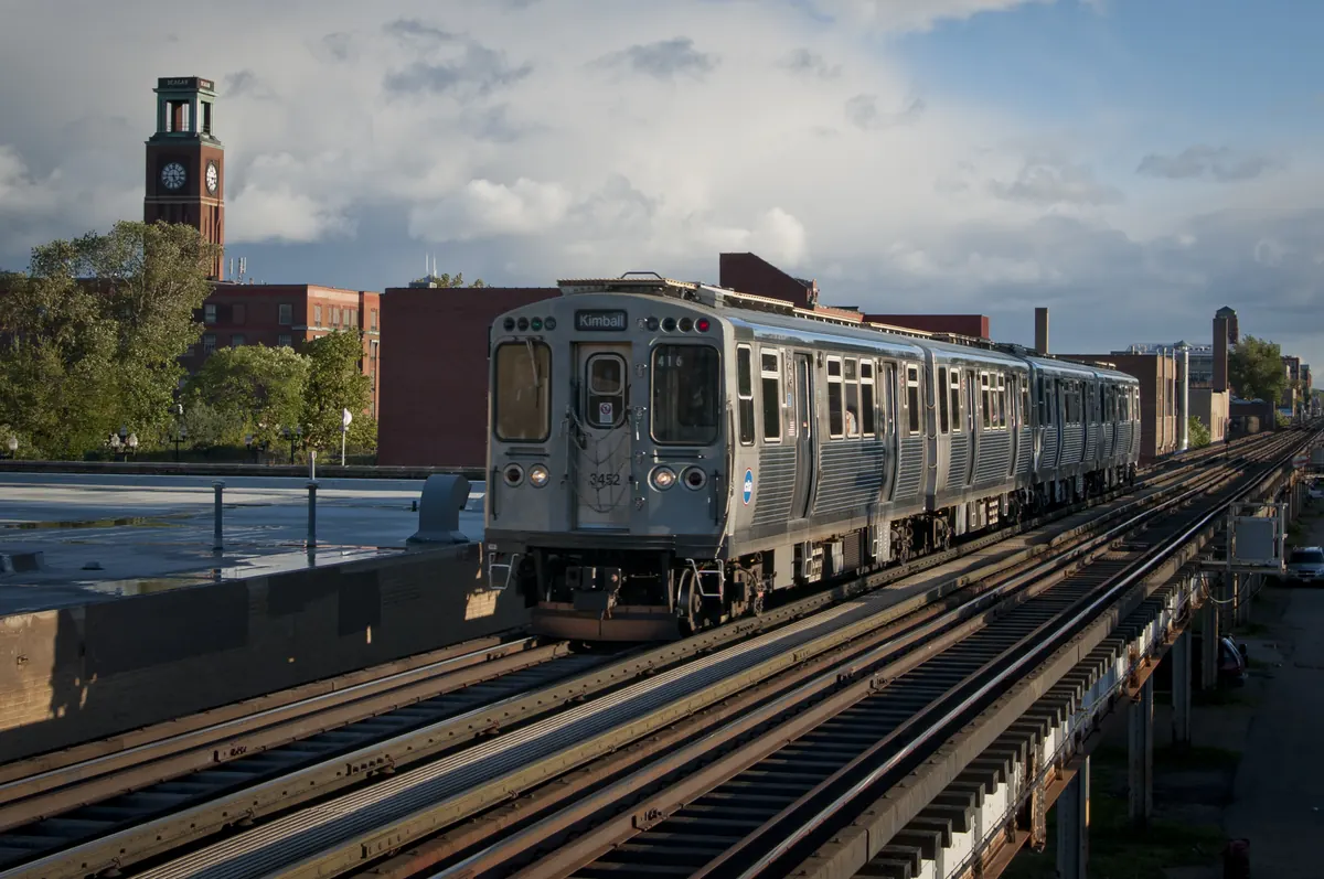 CTA Brown Line train on the elevated tracks in Ravenswood, Chicago, with brick buildings and a clock tower behind it