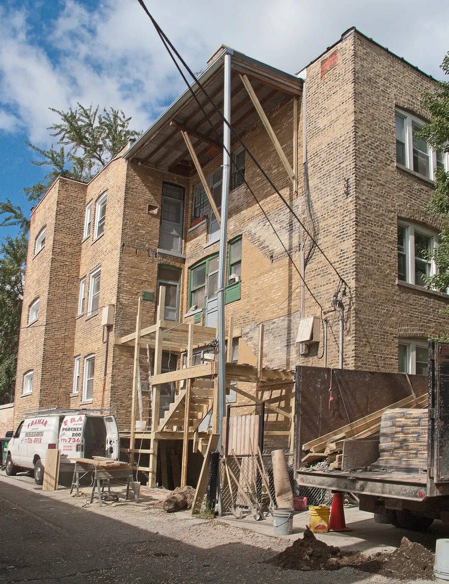 New wood back porch framing under construction on the rear of a yellow brick apartment building in Rogers Park, Chicago