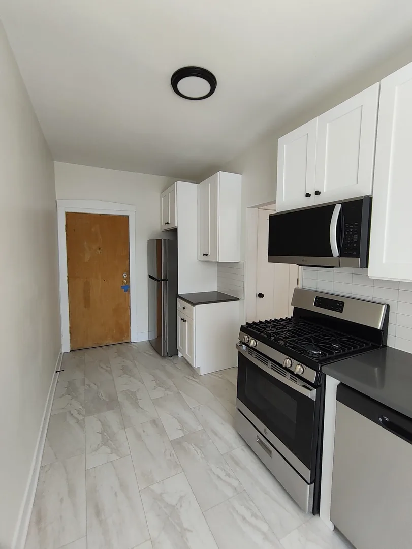Narrow renovated kitchen with white cabinets, a gas range, microwave and light tile floor in a Rogers Park apartment