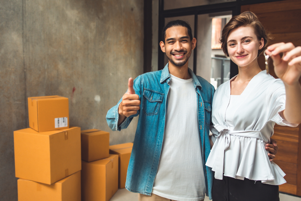 happy couple holding house keys with moving boxes