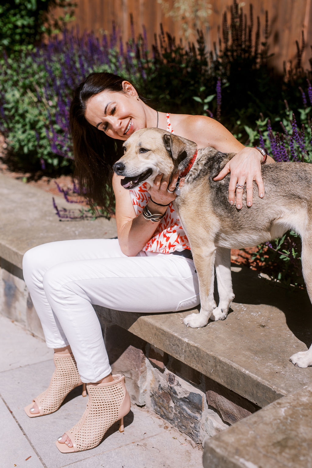a woman with dark hair looks lovingly at a medium sized dog with blonde fur