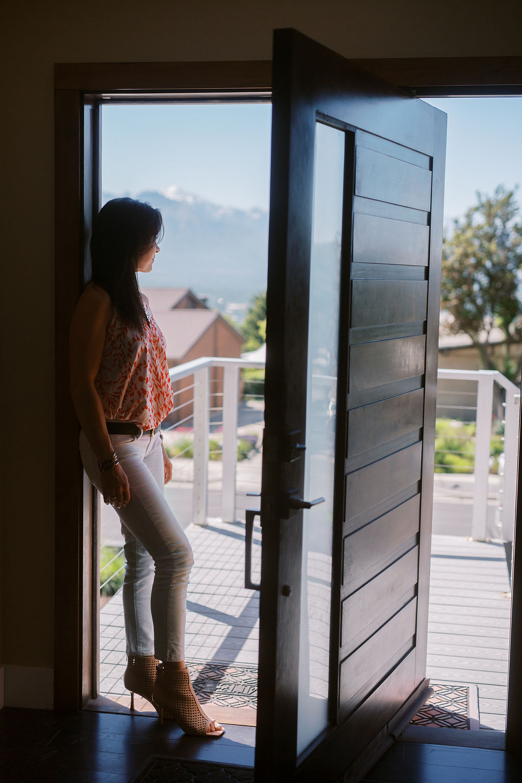 a woman with dark hair and a red shirt stands int eh doorway of her modern home