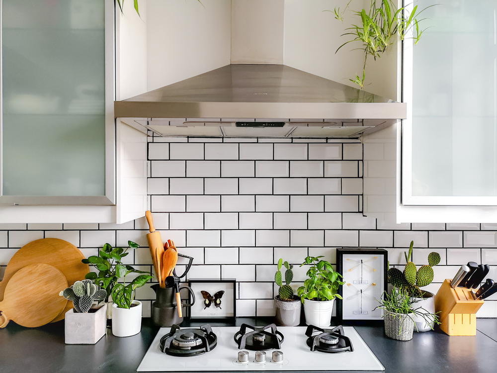 a nice looking white and black kitchen with cooking appliances, wooden utensils and cute houseplants