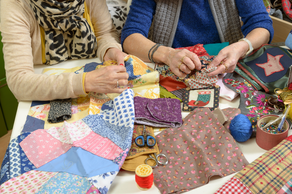 two women sewing a fabric creating a colorful patchwork